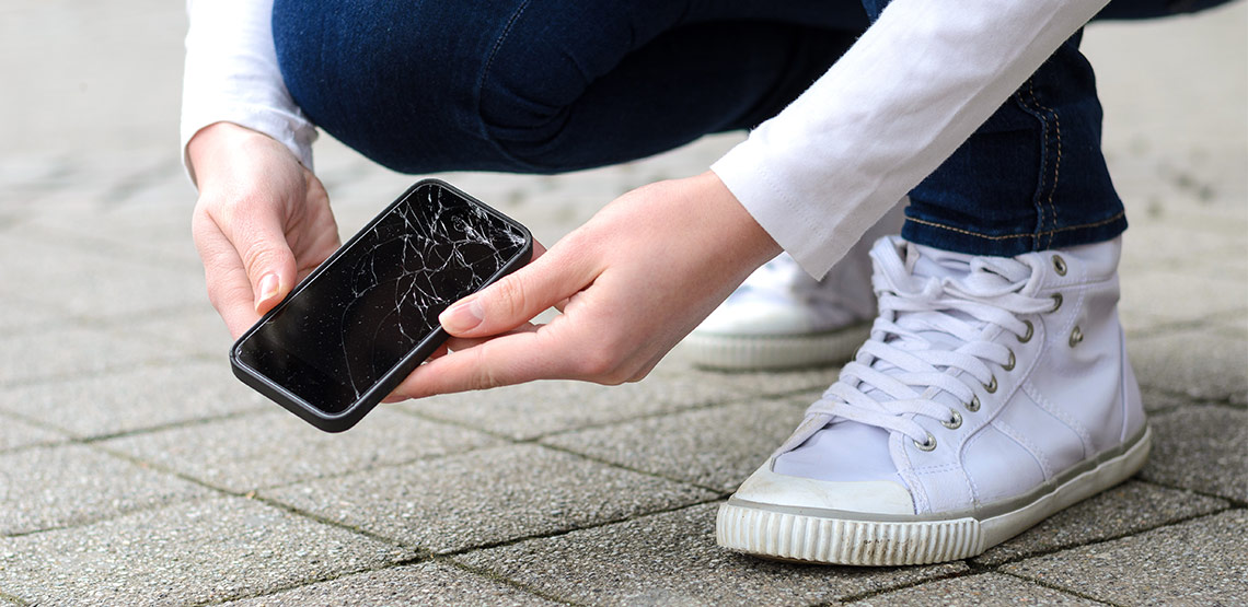 Someone picking their phone off the ground and it has a cracked screen