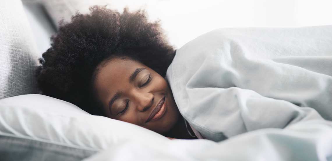 A person sleeping in bed with a duvet over them.