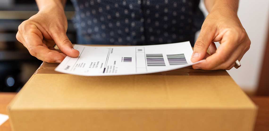 A person placing a shipping label on a cardboard box.