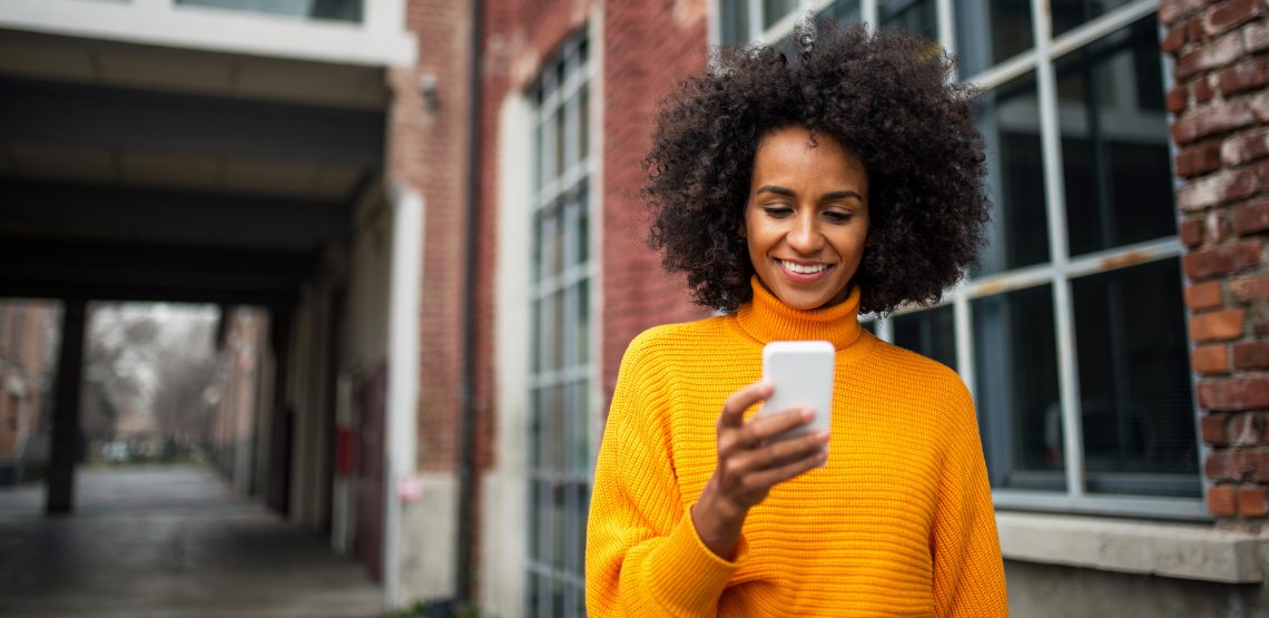 A woman in a yellow sweater holding a cell phone.